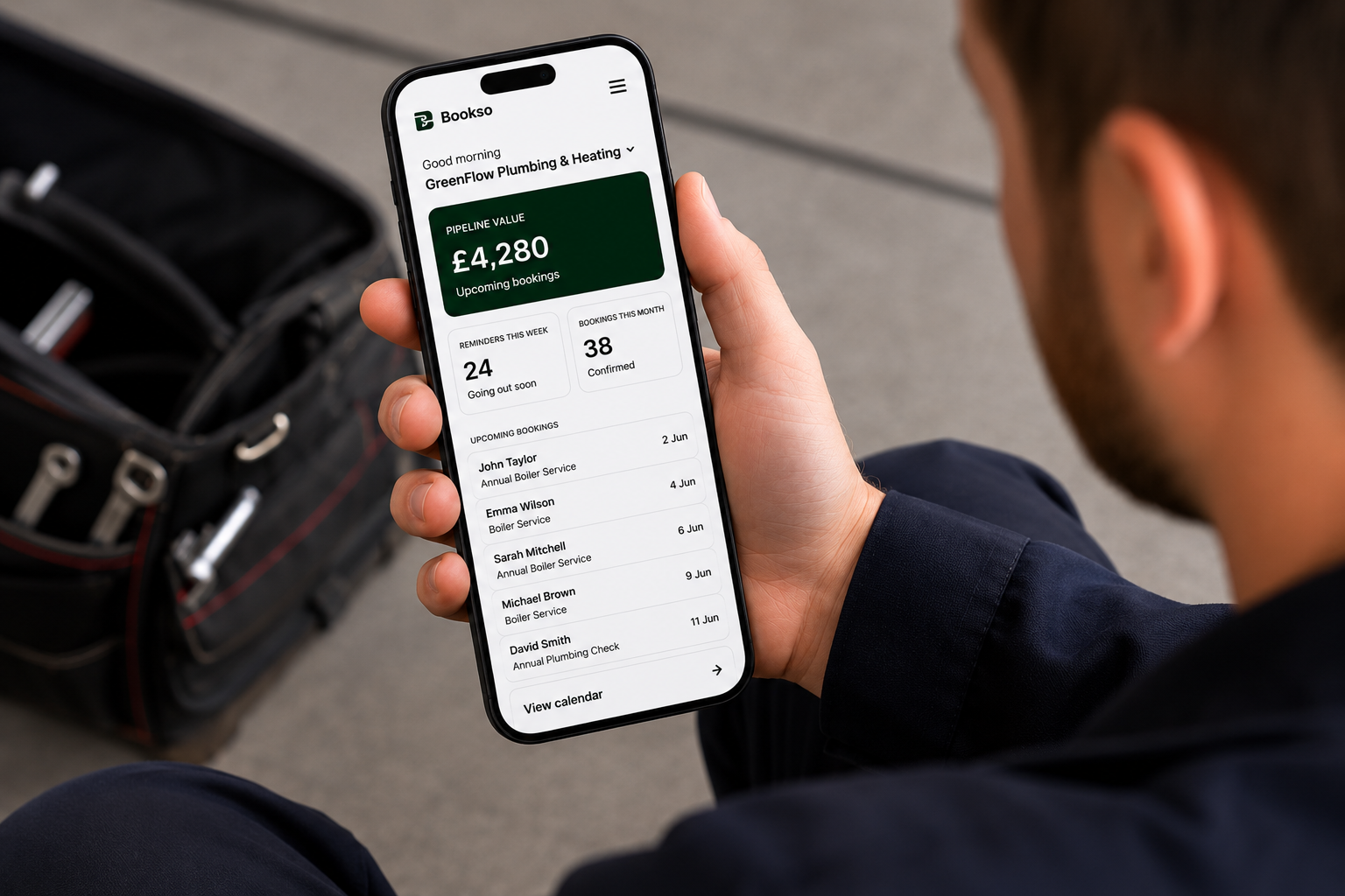 UK tradesperson reviewing the Bookso dashboard on their phone with a tool bag in the background